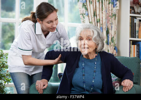 Lavoratore di cura di aiutare la donna Senior per arrivare fino al di fuori della sedia Foto Stock