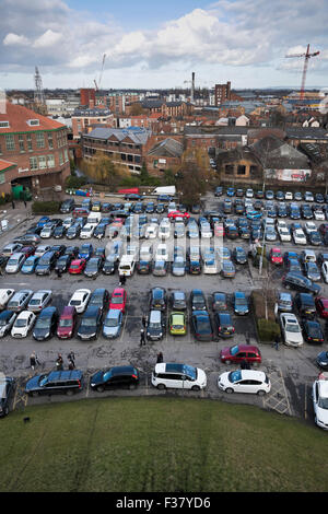 Alta Vista di York skyline (Inghilterra, Regno Unito) da la Torre di Clifford. La gente camminare & auto parcheggiata in un affollato, affollato di castello parco auto, gli edifici della città al di là. Foto Stock