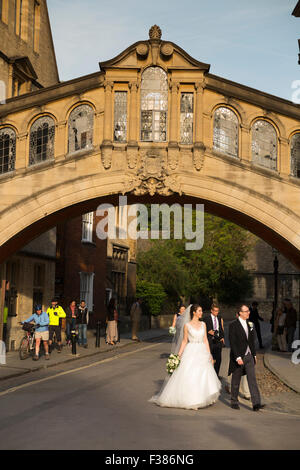 Coppie in viaggio di nozze a piedi al di sotto del ponte di Hertford, conosciuto popolarmente come il Ponte dei Sospiri, New College Lane, Oxford, Oxfordshire, Regno Unito. Foto Stock