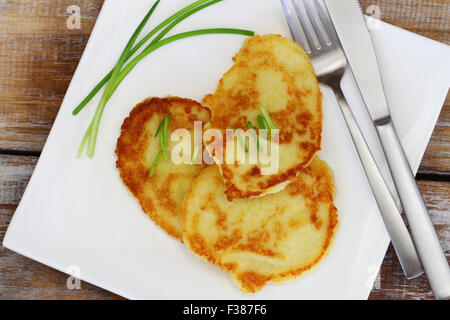 Frittelle di patate guarnite con cipolline sulla piastra bianca su rustiche superficie in legno Foto Stock