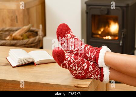 Donna in calze di Natale rilassante accanto a una stufa a legna Foto Stock