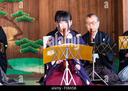 Kyoto, il santuario Yasaka, Noh prestazioni. Giovane donna giapponese inginocchiarsi durante la riproduzione nohkan, flauto, con giocatori maschi dietro di lei, su Honbutai, lo stadio. Foto Stock