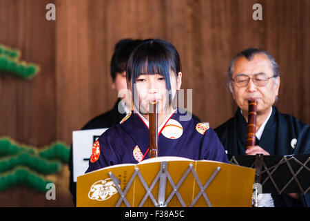 Kyoto, il santuario Yasaka, Noh prestazioni. Giovane donna giapponese inginocchiarsi durante la riproduzione nohkan, flauto, con giocatori maschi dietro di lei, su Honbutai, lo stadio. Foto Stock