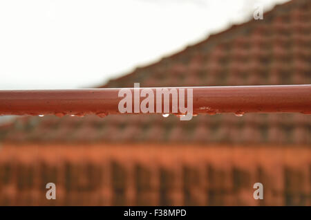 Gocce di pioggia sulla barra di metallo con un tetto rosso in background Foto Stock