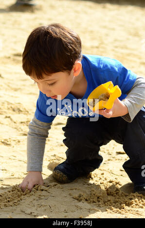 Un giovane ragazzo gioca con la sabbia in giochi per bambini area in parco. Foto Stock