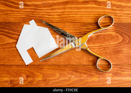 Forbici e casa tagliato fuori la carta sullo sfondo di legno Foto Stock