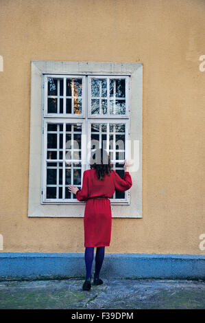 Donna in piedi al di fuori della casa guardando attraverso la finestra Foto Stock