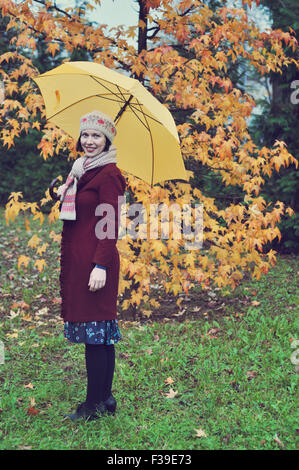 Donna in piedi nel parco azienda ombrello Giallo autunno Foto Stock