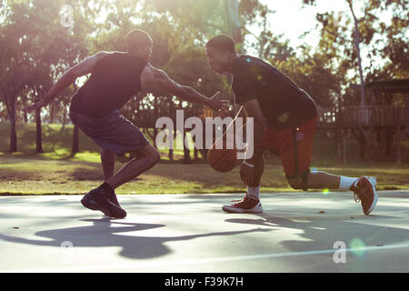 Due giovani uomini giocare a basket nel parco al tramonto Foto Stock