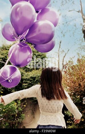 Vista posteriore di una ragazza con un mazzo di palloncini viola Foto Stock