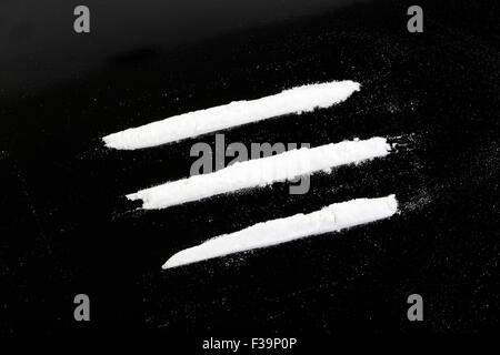 La cocaina in polvere in tre linee su uno sfondo nero Foto Stock
