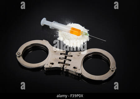 La cocaina farmaci heap con siringa e manette su uno sfondo nero Foto Stock