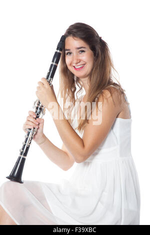 Bruna giovane donna vestita di bianco si trova in studio e trattiene il clarinetto sorridente Foto Stock