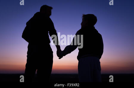 La promozione e il concetto di parenting foto di un padre e figlio in silhouette tenendo le mani a guardare il tramonto Foto Stock