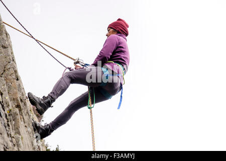 Female Rock scalatore la discesa in corda doppia con la fune di sicurezza e cablaggio di arrampicata su un rockface. Il Galles del Nord, Regno Unito, Gran Bretagna Foto Stock