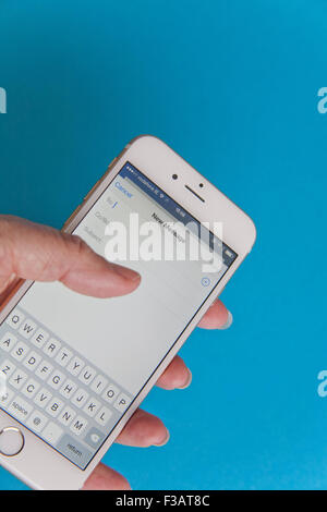 Invio di un messaggio di posta elettronica su un oro e bianco Apple iPhone 6 contro uno sfondo blu Foto Stock