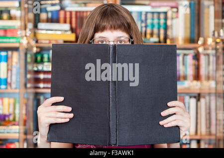 Ragazza con gli occhiali legge big book con coperchio cieco nella libreria Foto Stock