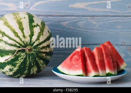 Una piastra di tagliare con cautela acqua pezzi di melone su un blu di tavole di legno dello sfondo. Foto Stock