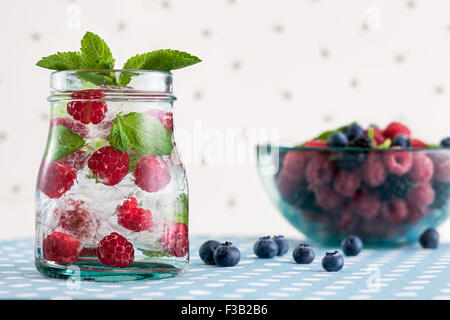 Lamponi freschi mojito e una ciotola di vetro con frutti di bosco su un bianco polka-sfondo puntinato Foto Stock