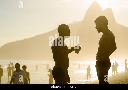 RIO DE JANEIRO, Brasile - 20 gennaio 2014: due giovani uomini hanno una conversazione in piedi in silhouette contro due fratelli Mt. Foto Stock