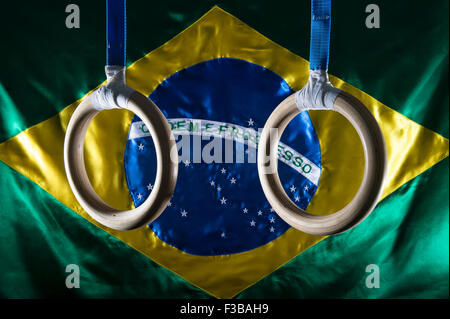 Anelli ginnasta appeso davanti di lucido bandiera brasiliana sfondo Foto Stock