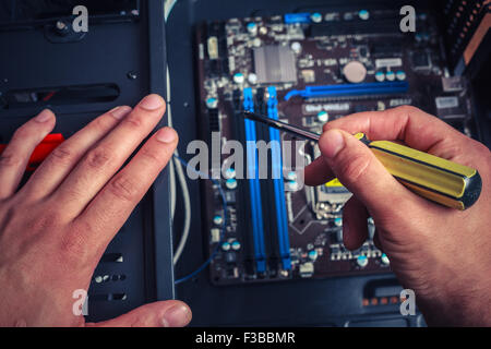 Una mano che tiene un cacciavite è l'installazione o la riparazione dei componenti del computer Foto Stock