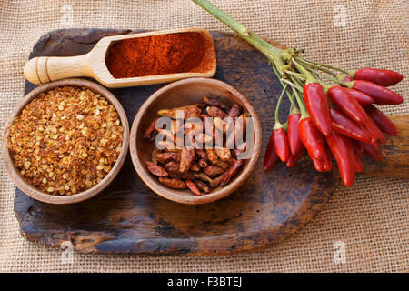 Peperoncino, cialde fresche su un mazzetto, essiccato in ciotola di legno, frantumata in una ciotola di legno e la polvere di legno sul convogliatore è tutto su un o Foto Stock