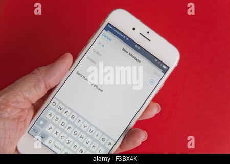 Invio di un messaggio di posta elettronica su un oro e bianco Apple iPhone 6 contro uno sfondo rosso Foto Stock