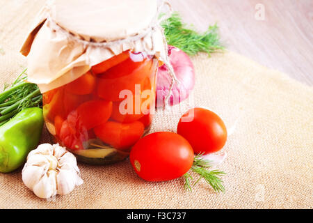 Pomodori marinati in vasetti con spezie e verdure su un tavolo di legno Foto Stock