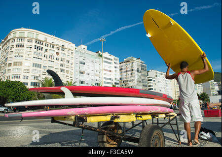 Giovane brasiliano uomo scarica le tavole da surf da un carrello sul lungomare a spiaggia di Copacabana a Rio de Janeiro in Brasile Foto Stock