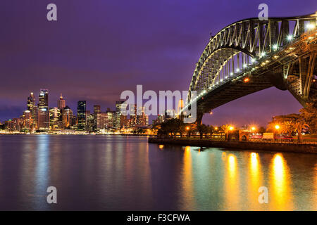 Sydney CBD cityline illuminata di edifici ad alta e Harbour Bridge con colorate in riflessione sfocata acque del porto Foto Stock