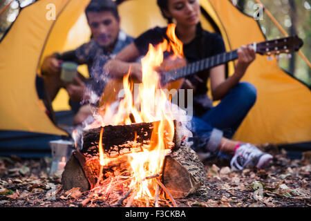 Ritratto di una giovane coppia seduta con chitarra vicino falò in foresta Foto Stock