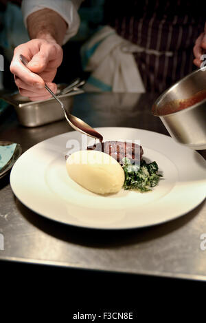 Ristorante lo chef versando in salsa di carne e il piatto di patate Foto Stock