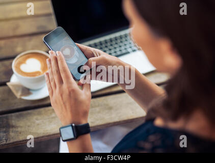 Immagine ravvicinata di donna fotografare un caffè di cup con il suo telefono cellulare mentre è seduto in un bar.