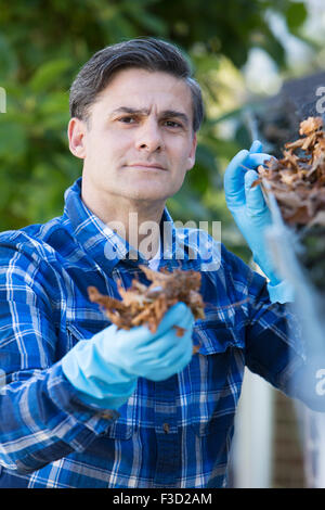 Uomo di foglie di compensazione dalla grondaia della casa Foto Stock