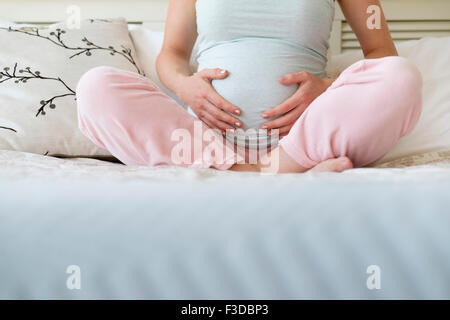 Donna incinta seduta sul letto Foto Stock