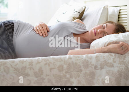 Donna incinta dorme nel letto Foto Stock