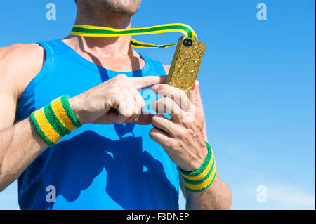 Atleta brasiliano con il verde ed il giallo polsini con medaglia d oro telefono mobile contro il cielo blu Foto Stock