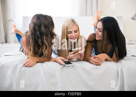 Ritratto di tre amiche giacente sul letto con lo smartphone a casa Foto Stock