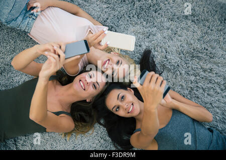 Vista dall'alto il ritratto di tre amiche utilizzando smartphone sul tappeto a casa Foto Stock