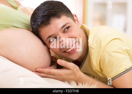 Il marito ascoltando la pancia di sua moglie incinta Foto Stock