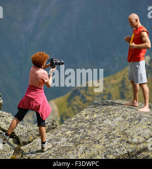 Donna con foto professionali fotocamera di scattare la foto di un uomo sportivo sulle montagne Foto Stock