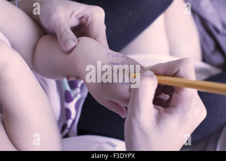 Madre la scrittura sul bambino la mano, ritagliato Foto Stock