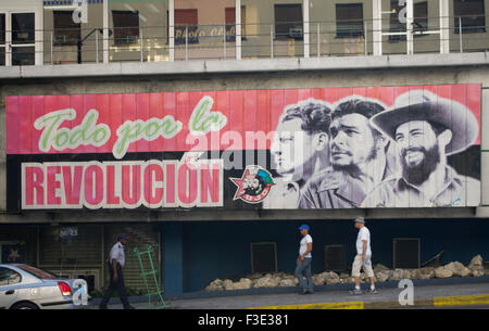 Persone in Havana Cuba a piedi passato un segno tradotto come tutto per la Rivoluzione, raffigurante Fidel Castro e altri due uomini. Foto Stock