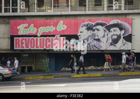 Persone in Havana Cuba a piedi passato un segno tradotto come tutto per la Rivoluzione, raffigurante Fidel Castro e altri due uomini. Foto Stock