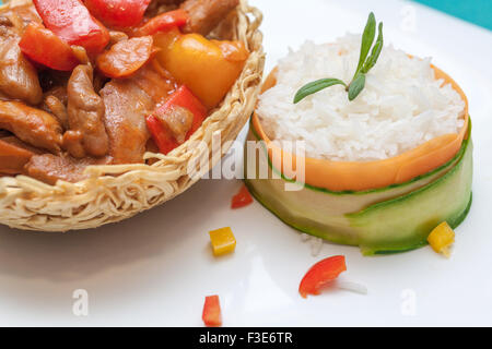 Piatto cinese; pollo con dolci peperoni verdi in un fritto a base di noodle nido e cotto a vapore luogo decorato con il cetriolo e la carota a parte Foto Stock