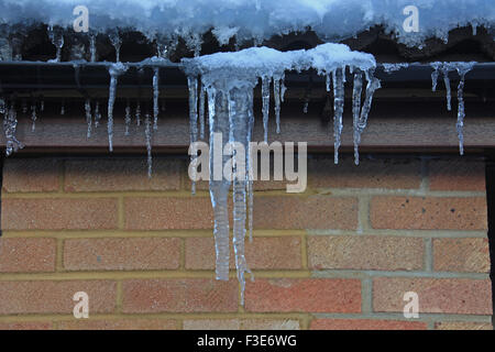 Grandi ghiaccioli incrostazione formata una grondaia della casa durante un inverno freddo Foto Stock