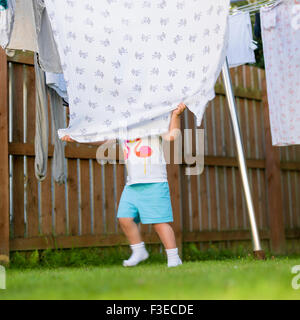 3 anno di età di nascondersi dietro una coperta sulla linea di lavaggio in giardino Foto Stock