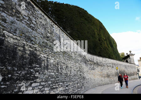 Due giovani ragazze a piedi lungo accanto alla massima Yew Tree, Taxus baccata, hedge nel Regno Unito. Si trova proprio sul Bathurst Esate vicino a Cirencester, Regno Unito Foto Stock