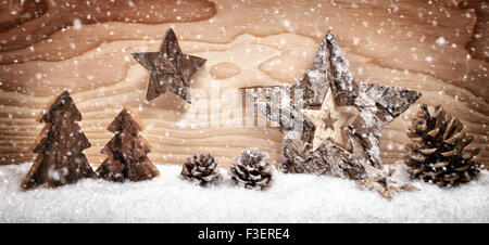 Festa di Natale la disposizione con splendidi ornamenti di legno sulla neve nella parte anteriore di un brillante pannello di legno sfondo, studio shot Foto Stock